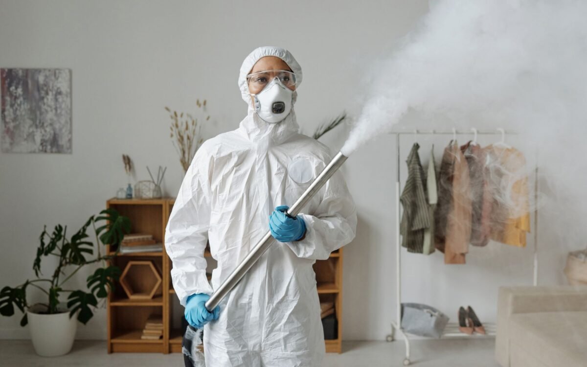 Uma pessoa em equipamento de proteção completo fumiga o interior para desinfecção