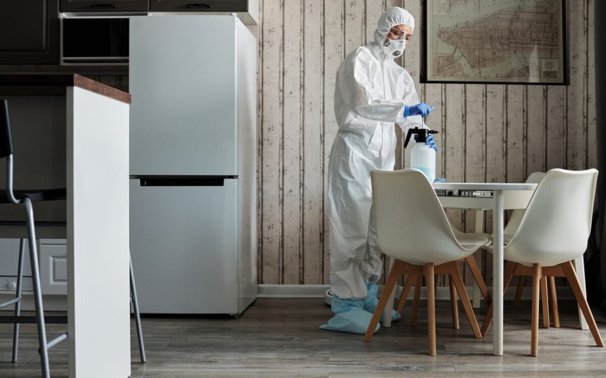 Pessoa em traje de proteção desinfetando uma mesa de cozinha moderna com spray para higiene