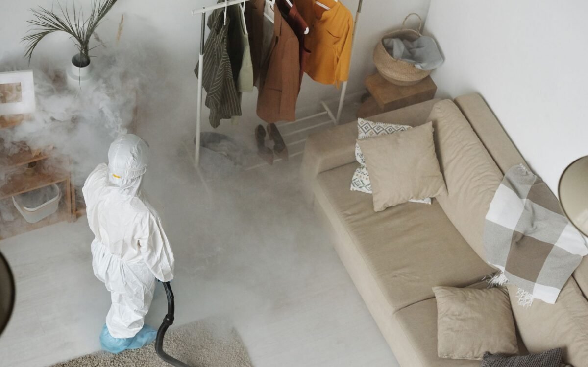 Profissional em equipamento de proteção sanitizando uma sala de estar moderna com máquina de fumigação