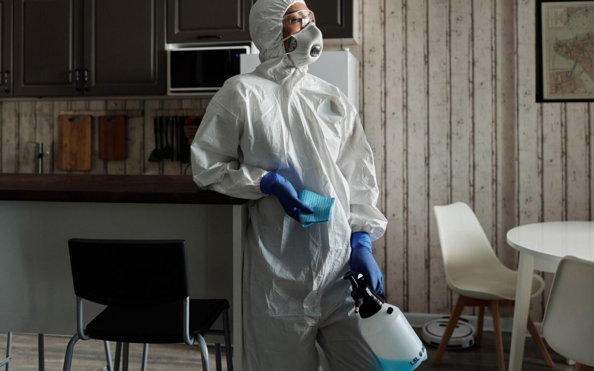 Limpador em traje de proteção usando um pulverizador para desinfecção em ambientes. Foco em segurança e higiene