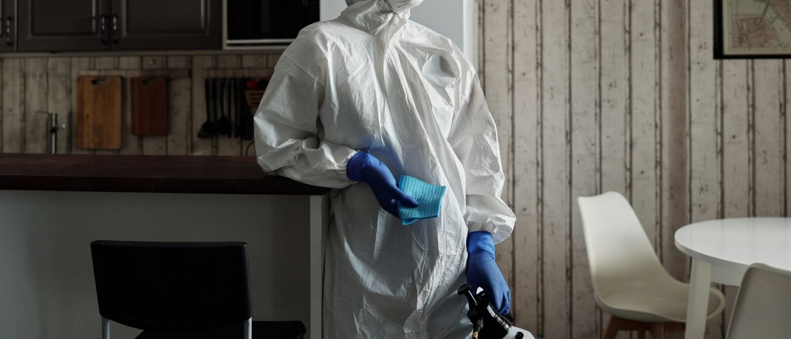 Limpador em traje de proteção usando um pulverizador para desinfecção em ambientes. Foco em segurança e higiene