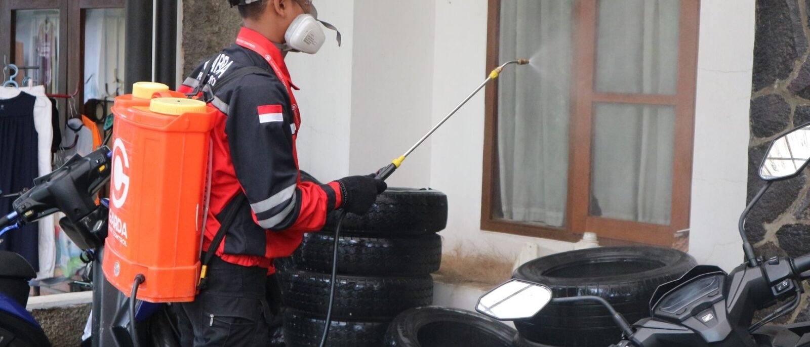Um trabalhador em equipamento de segurança pulveriza desinfetante fora de um edifício, garantindo limpeza