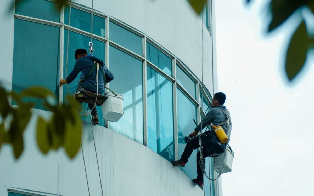 Limpadores de janelas suspensos por cordas limpam a fachada de vidro de um edifício alto