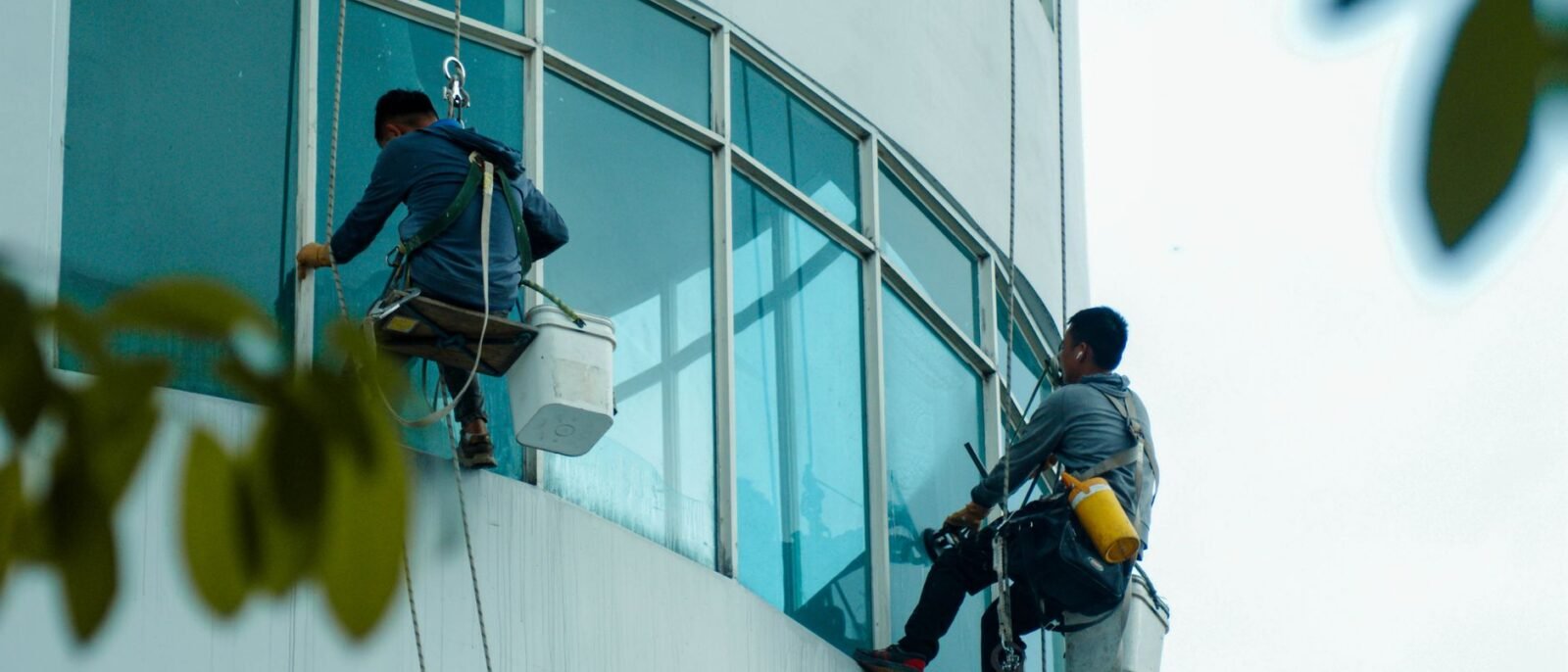 Limpadores de janelas suspensos por cordas limpam a fachada de vidro de um edifício alto