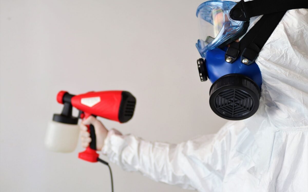 Um trabalhador em equipamento de proteção usa um spray desinfetante em ambientes fechados