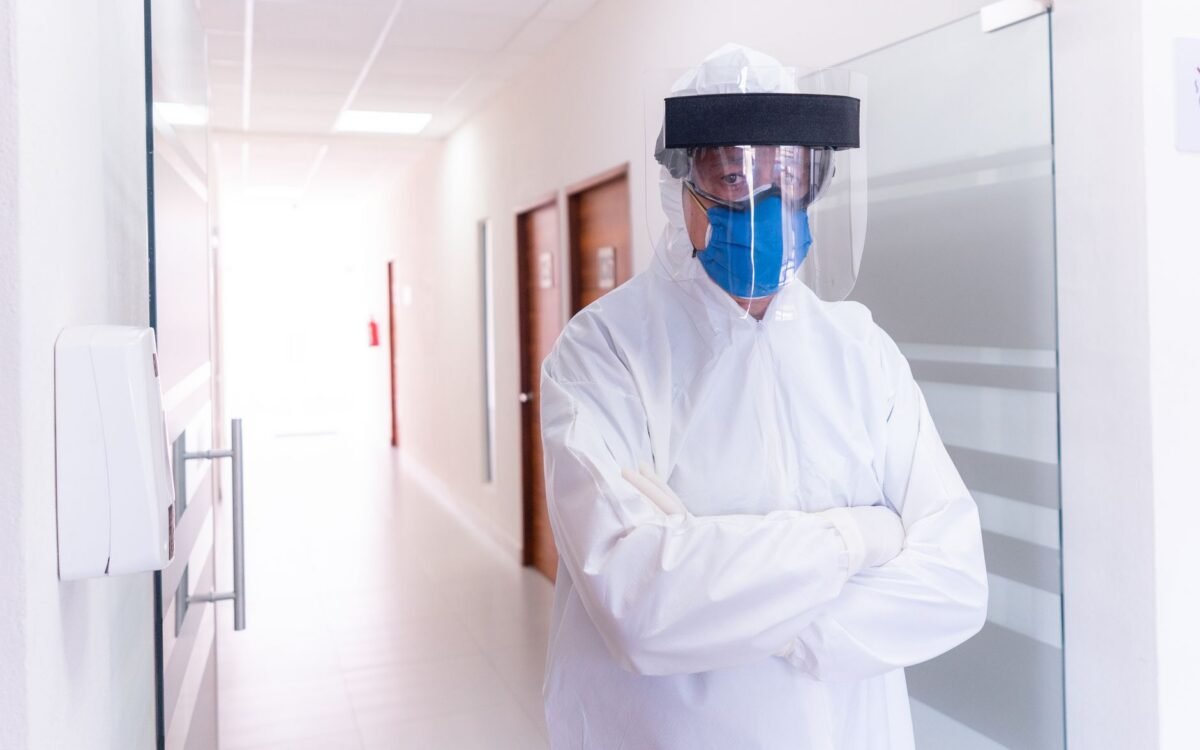 Profissional de saúde em corredor de hospital usando equipamento de proteção completo, máscara e protetor facial