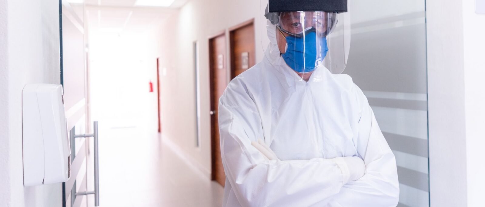 Profissional de saúde em corredor de hospital usando equipamento de proteção completo, máscara e protetor facial
