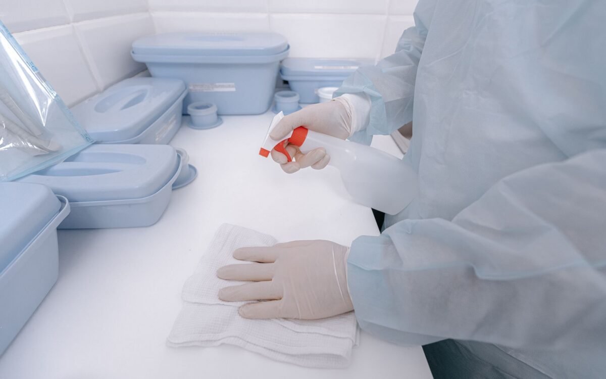 Um profissional de saúde usando luvas sanitiza uma superfície com um frasco pulverizador em um ambiente médico