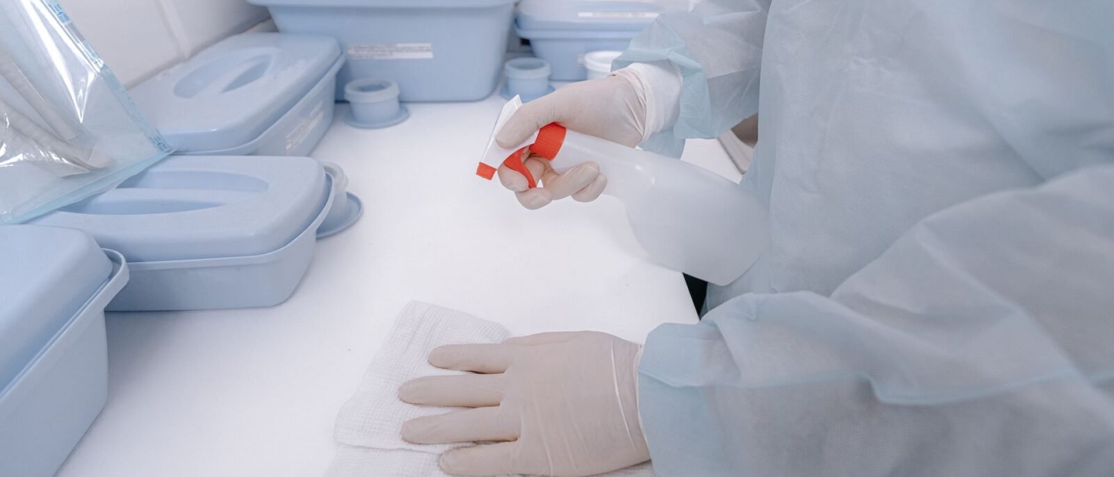 Um profissional de saúde usando luvas sanitiza uma superfície com um frasco pulverizador em um ambiente médico