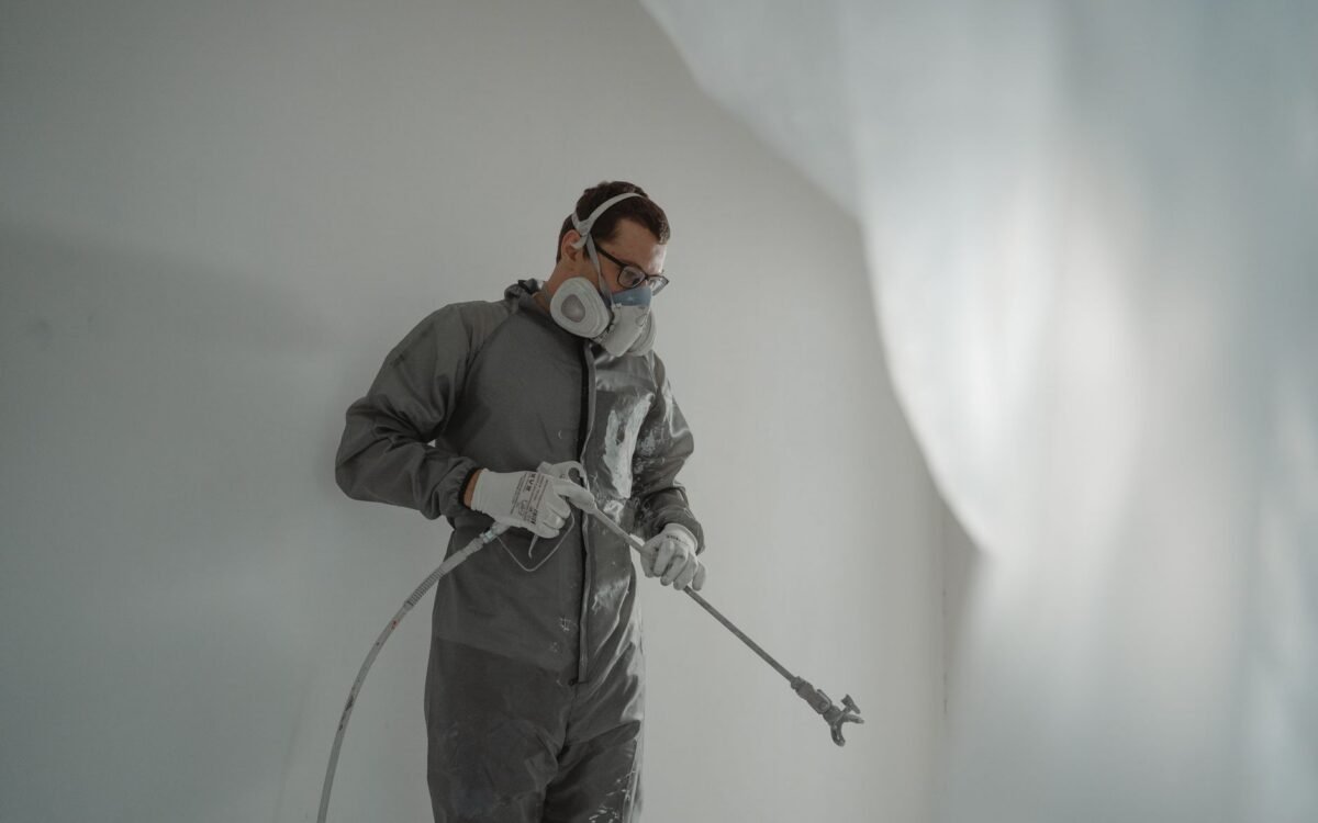 Pessoa em equipamento de proteção pintando uma parede, mostrando trabalho de renovação residencial