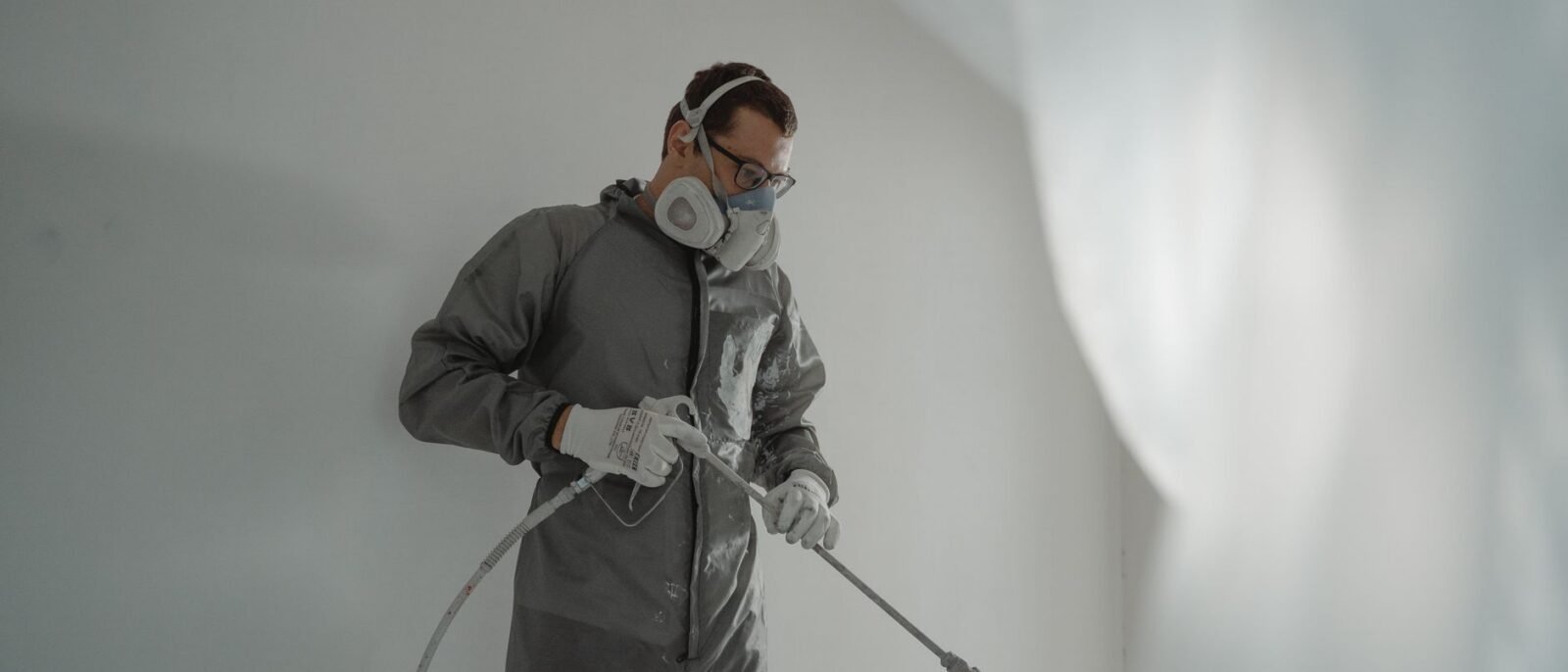 Pessoa em equipamento de proteção pintando uma parede, mostrando trabalho de renovação residencial